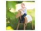Petite fille souriante assise sur un cheval à bascule en bois à l'extérieur.