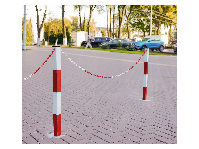 Deux poteaux avec une chaîne blanche et rouge délimitent un espace sur une rue pavée.