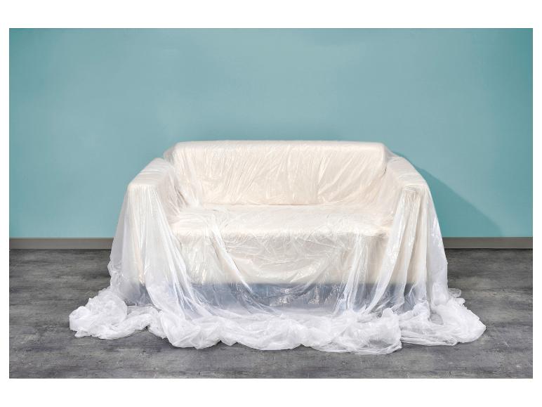 Canapé recouvert de plastique de protection devant un mur bleu et un sol en béton