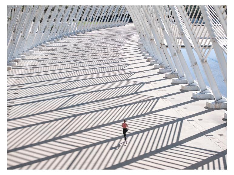 Femme courant sur un pont avec des structures métalliques blanches et de longues ombres