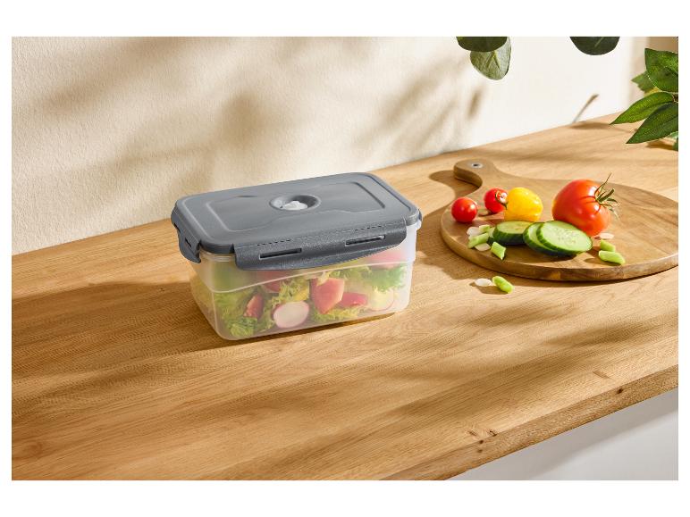 Récipient sous vide avec salade sur un comptoir en bois, à côté de légumes sur une planche à découper.