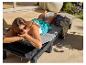 Une femme se relaxe sur une chaise longue en résine tressée grise avec coussin gris ; détente ensoleillée.