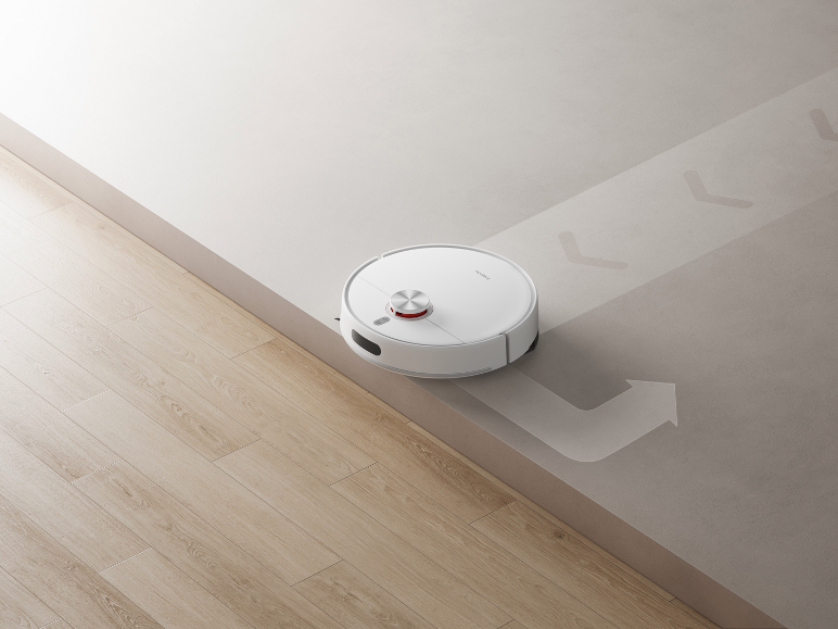 Robot aspirateur blanc nettoyant le long du rebord d'une marche.