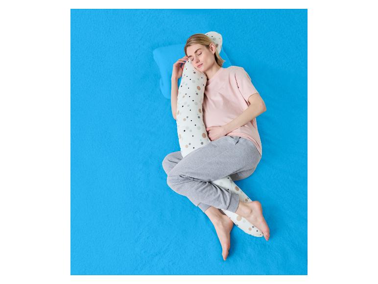 Femme dormant sur le côté avec un oreiller de corps sur un drap bleu.