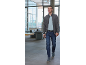 Homme en cardigan gris, polo bleu clair, jean et chaussures bleues marchant dans un intérieur moderne.