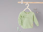 Un t-shirt bébé vert clair à manches longues, suspendu à un cintre en bois.