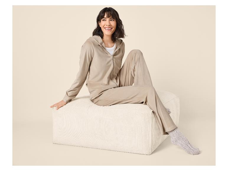 Femme en survêtement en velours beige et chaussettes tricotées assise sur un pouf.