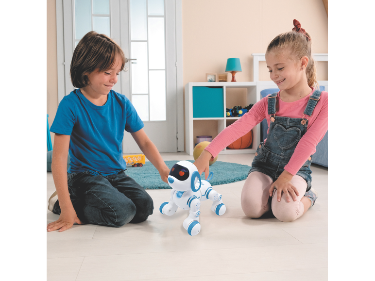 Deux enfants jouent avec un chiot robot blanc et bleu sur le sol.