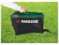 Une main tient un bac de ramassage d'herbe vert avec un sac en filet noir sur une pelouse.
