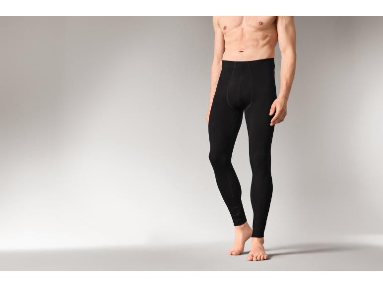 Un homme portant un legging thermique noir, debout sur fond gris.