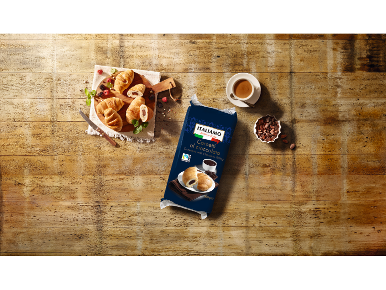 Croissants au chocolat sur une planche en bois avec des baies, du café et un paquet de croissants.