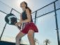 Femme en tenue de sport avec raquette de padel sur un court, souriante et regardant vers le haut.