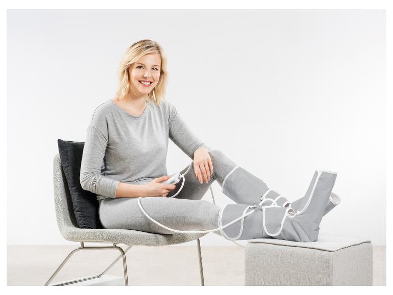 Femme assise sur une chaise avec un appareil de massage des jambes, souriante.