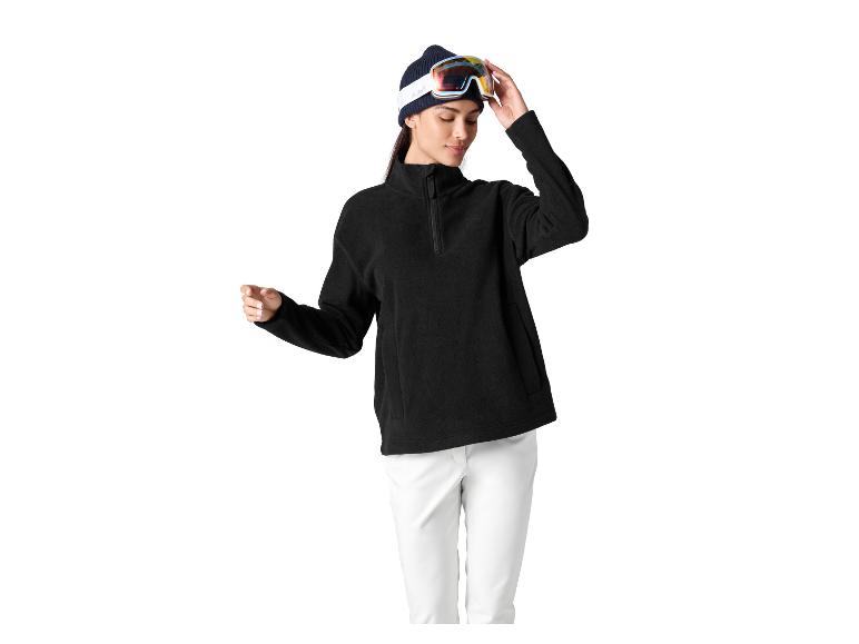 Femme en polaire noire, pantalon blanc et lunettes de ski sur bonnet.