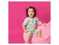 Enfant heureux en barboteuse rayée assis sur une chaise rose moelleuse.