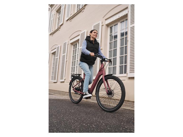 Une femme roule à vélo électrique rose avec un porte-bagages.