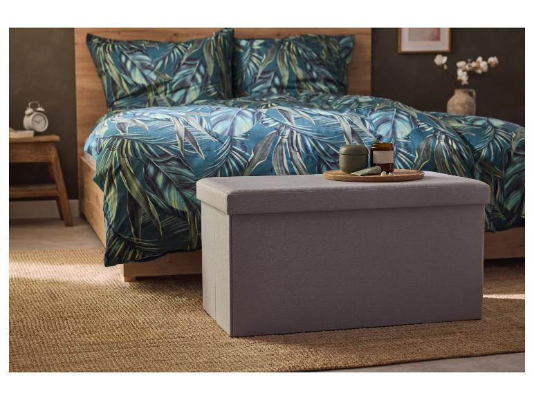 Un pouf de rangement en tissu gris se trouve sur un tapis en jute dans une chambre à coucher avec un lit au style tropical.