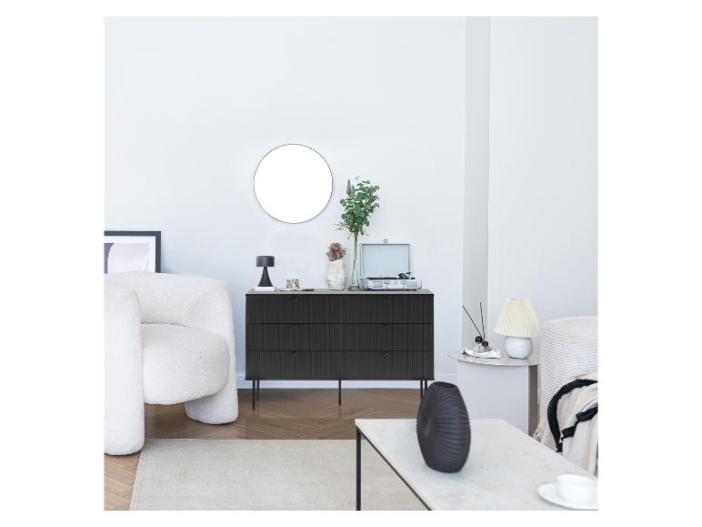 Commode noire, miroir rond, fauteuil blanc et tourne-disque dans un salon.