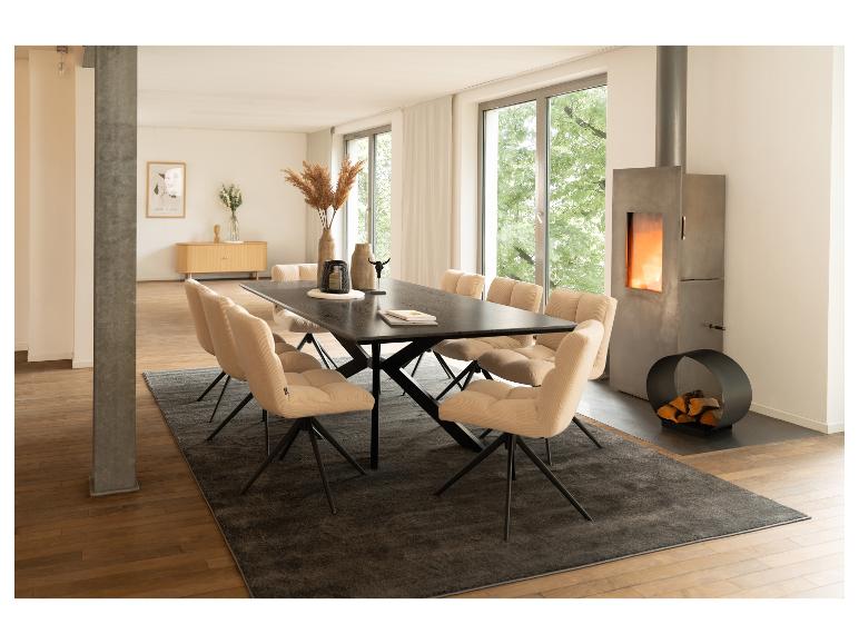 Salle à manger moderne avec table noire, chaises beiges et cheminée en béton.