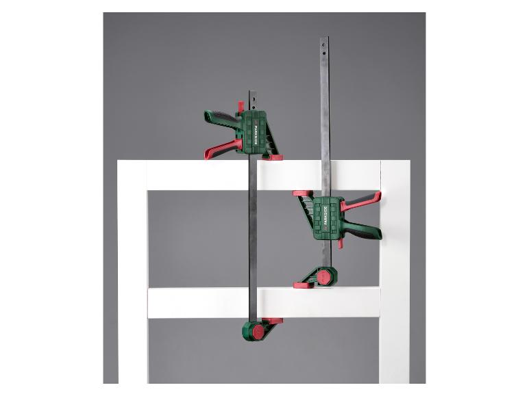 Deux serre-joints de menuiserie verts et rouges fixés sur un cadre blanc.