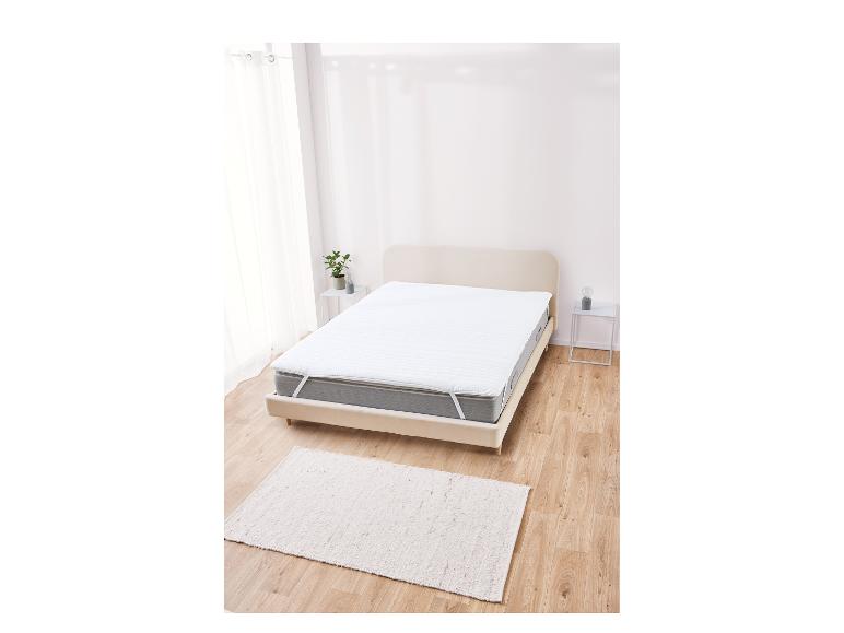 Protège-matelas blanc avec élastiques sur un lit en bois clair.