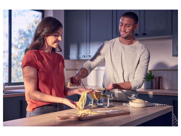 Couple préparant des pâtes fraîches avec une machine à pâtes dans une cuisine moderne.