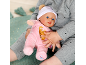 Un enfant tient un poupon vêtu d'un pyjama rose et d'un bonnet blanc.