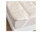 Surmatelas doux en laine de mouton crème sur un lit blanc.