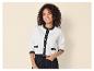 Femme souriante portant un cardigan blanc et noir avec des boutons dorés et un pantalon noir.