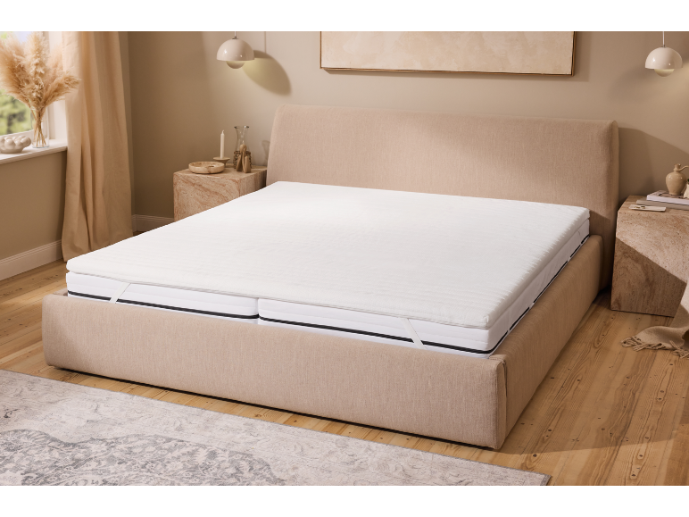 Lit beige avec matelas et surmatelas blanc dans une chambre au sol en bois.