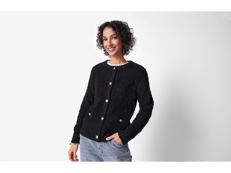 Femme souriante en cardigan noir texturé et jean, main dans la poche.