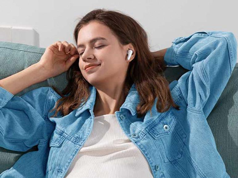 Femme se relaxant sur un canapé, écoutant de la musique avec des écouteurs intra-auriculaires blancs.