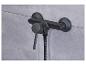 Un mitigeur de douche noir avec un bouton de thermostat sur un mur en carrelage gris.