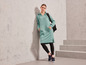 Une femme vêtue d'une robe sweat-shirt verte, de leggings noirs et de baskets.