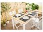 Table et chaises pliantes blanches, vaisselle et sets de table noirs pour un repas en extérieur.