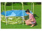 Une femme assemble une piscine gonflable avec un motif tropical et un parasol.