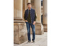 Un homme porte un gilet matelassé bleu, un pull vert et un jean bleu.