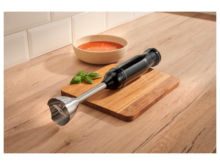 Mixeur plongeant noir sur une planche à découper en bois à côté d'un bol de soupe de tomates.