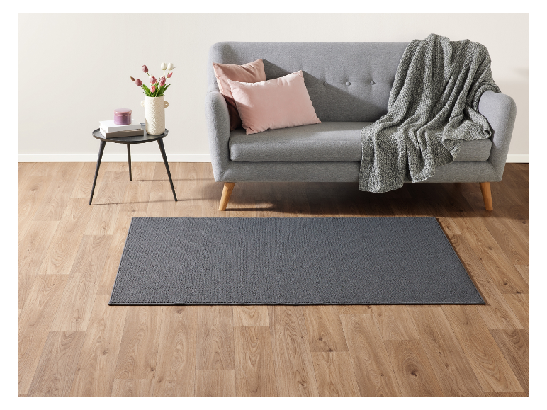 Tapis gris foncé sur un sol en bois clair, près d'un canapé gris.