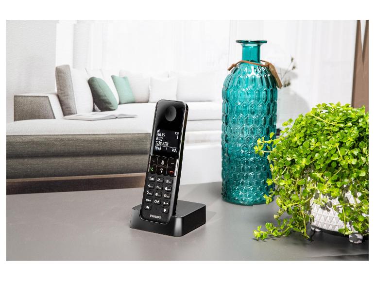 Téléphone sans fil avec station de charge sur une table, à côté d'un vase et d'une plante.
