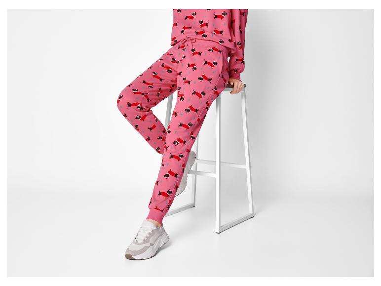 Femme assise sur un tabouret en pantalon de survêtement rose avec des teckels de Noël.