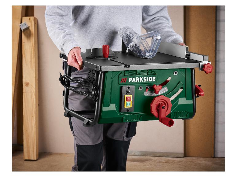 Personne portant une scie sur table verte avec une manivelle et des commandes rouges, prête pour le travail du bois.