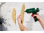 Des mains collent des plumes en bois sur un mur de briques blanches avec un pistolet à colle.