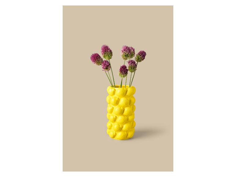 Vase jaune avec des fleurs violettes sur fond beige.