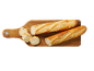 Deux baguettes et des morceaux de baguette tranchés sur une planche à découper en bois.