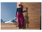 Une femme en tenue de ski avec des skis et un casque devant un fond en bois.