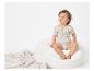 Bébé assis sur un pouf en fausse fourrure, vêtu d'un body à motifs tropicaux.