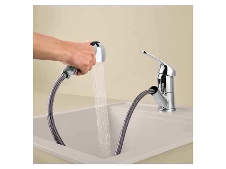 Robinet de cuisine avec douchette extractible dans un évier beige, avec de l'eau qui coule.