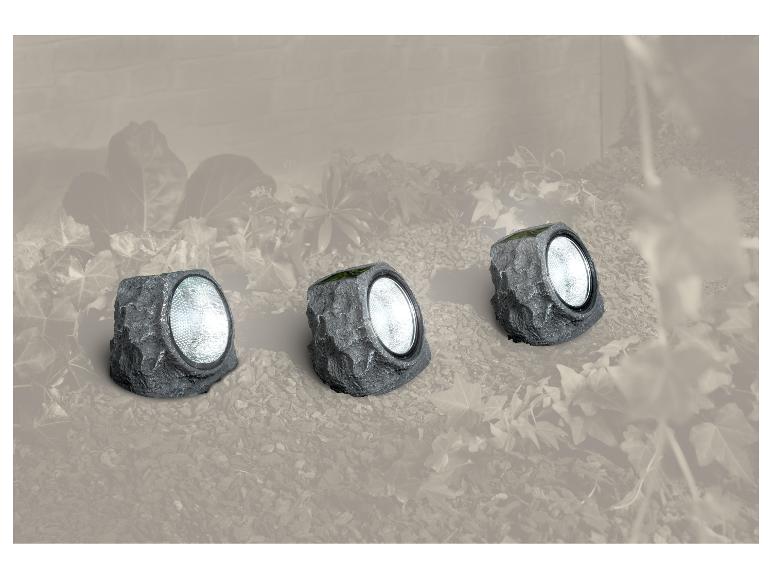 Trois lampes solaires de jardin grises en forme de roche, intégrées dans un environnement de jardin.