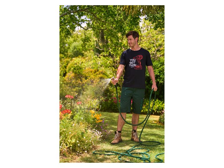 Homme en t-shirt noir et short vert arrosant des fleurs dans un jardin.
